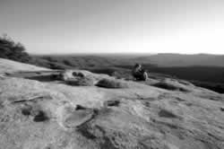 A hiker enjoys the view from the summit of Stone Mountain at Stone Mountain Park. Stone Mountain is a granite dome that rises 600 feet above the surrounding forests. A variety of domes are visible in the 13,000-acre park, which are the exposed sections of a 25-square mile pluton or large igneous rock that was formed underground and eventually exposed due to erosion.